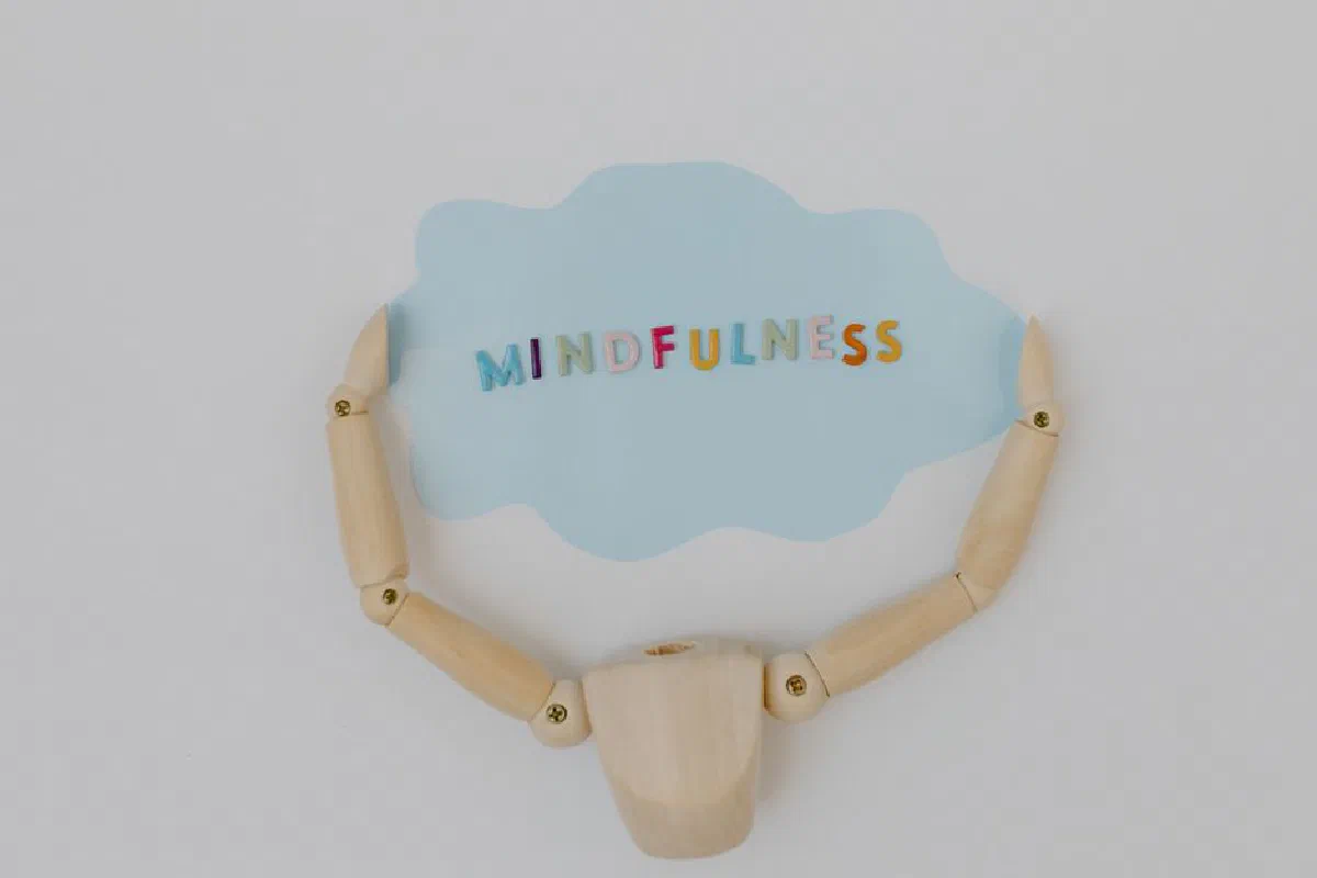 Wooden mannequin arms holding a blue cloud with 'Mindfulness' text, promoting self-awareness.
