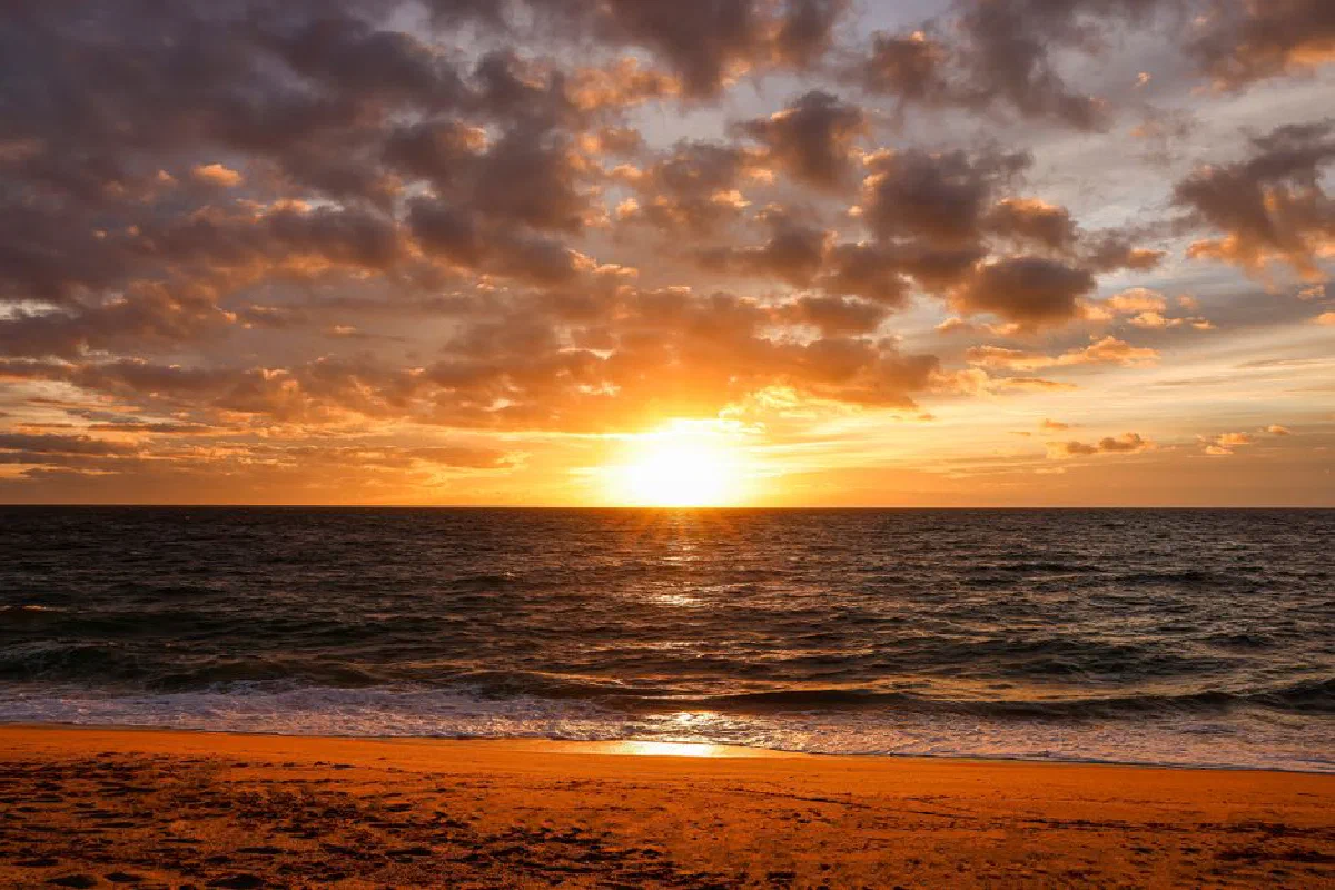 Beautiful sunset over the ocean with a sandy beach and dramatic sky.