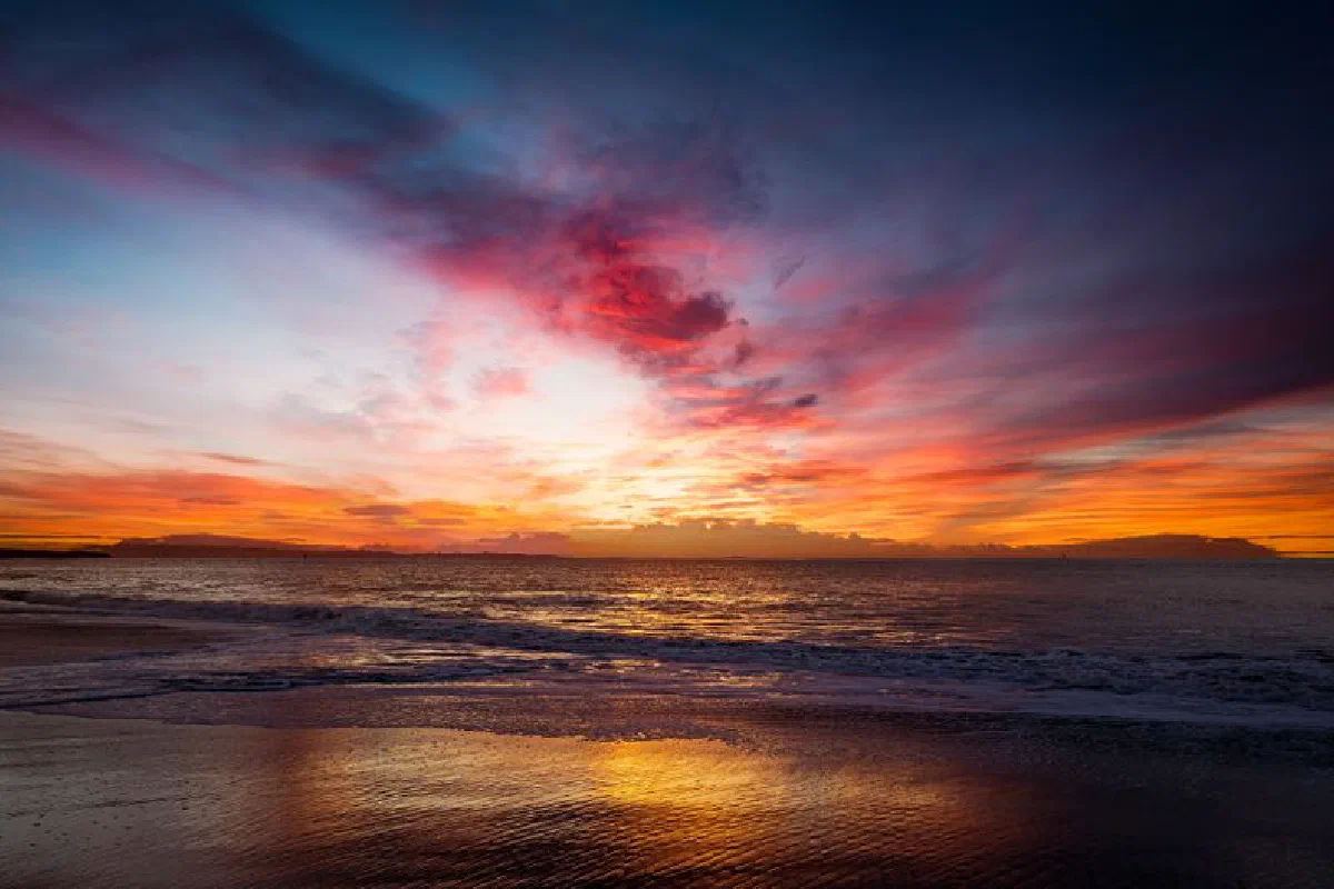 Breathtaking sunset creates a dramatic sky over the ocean with vibrant reflections on the shore.
