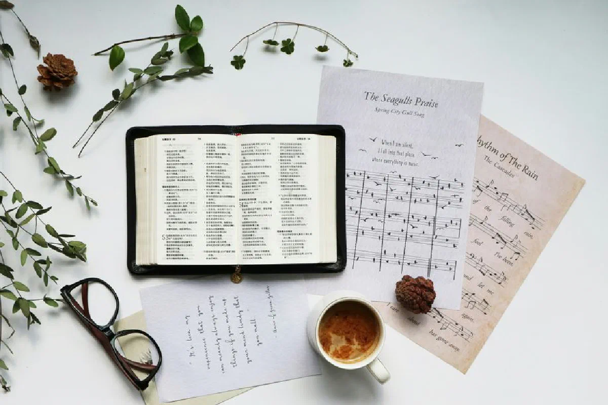 Top view of an open book with coffee, eyeglasses, and sheet music on a white background.
