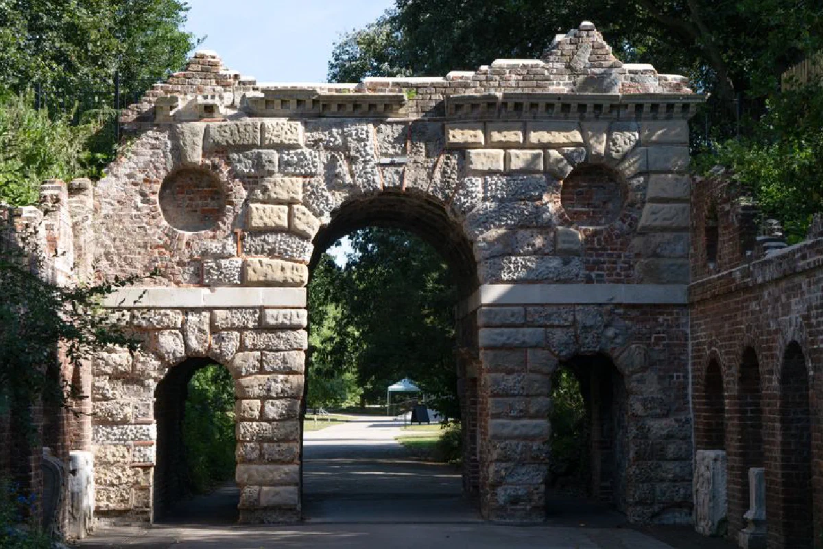 A sunlit view of a historic stone archway surrounded by lush greenery.