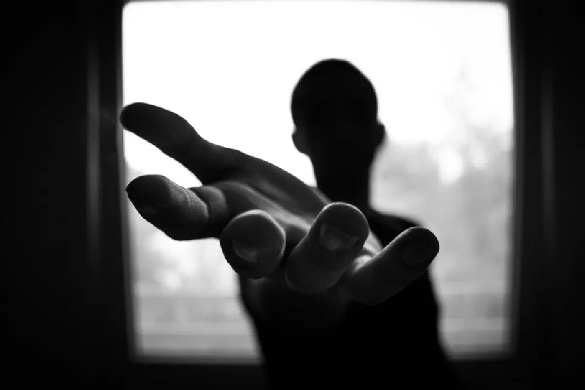 Silhouette of a hand reaching out in a black and white contrast.