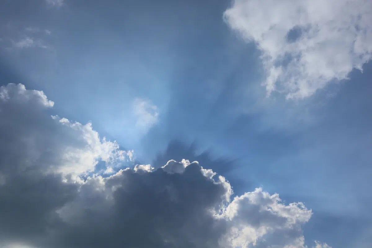 Majestic cumulus clouds with sun rays shining through a vibrant blue sky.