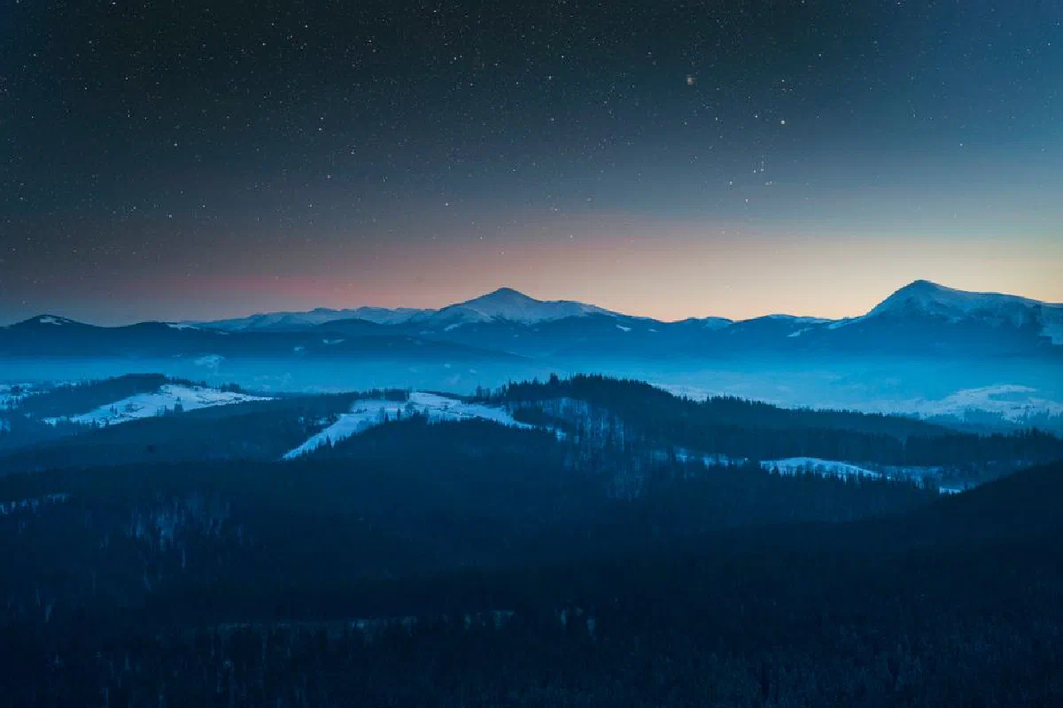 Breathtaking view of snow-covered mountains under a starry sky during twilight.