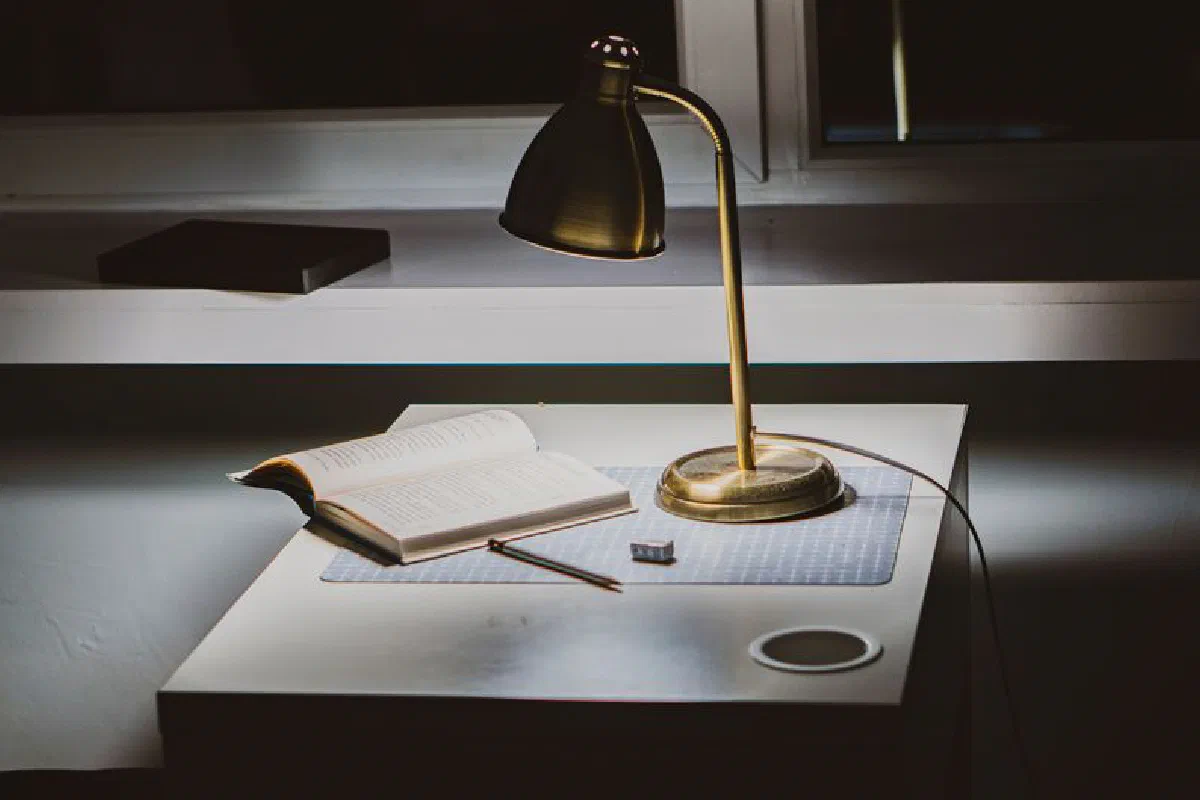A warm, inviting study space featuring a lamp, open book, and writing utensil on a modern desk.