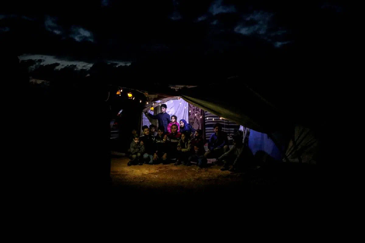 A family gathers under a tent at night, illuminated by warm lights in Idlib, Syria.