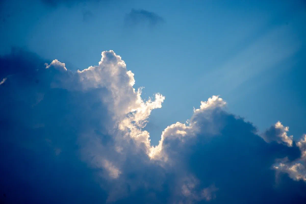 Sunlight streaming through cumulus clouds on a clear blue sky.
