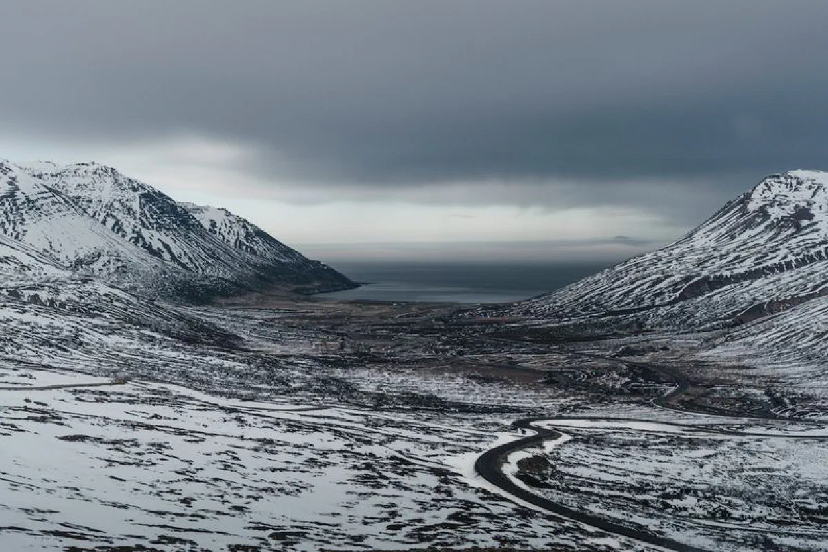 Breathtaking view of a snow-covered mountain valley in Iceland with a winding road below.