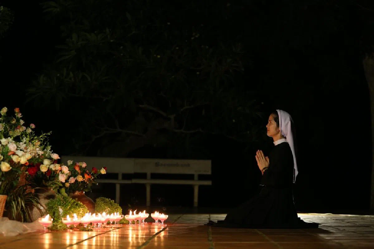 A nun praying by candlelight surrounded by flowers, symbolizing peace and faith.