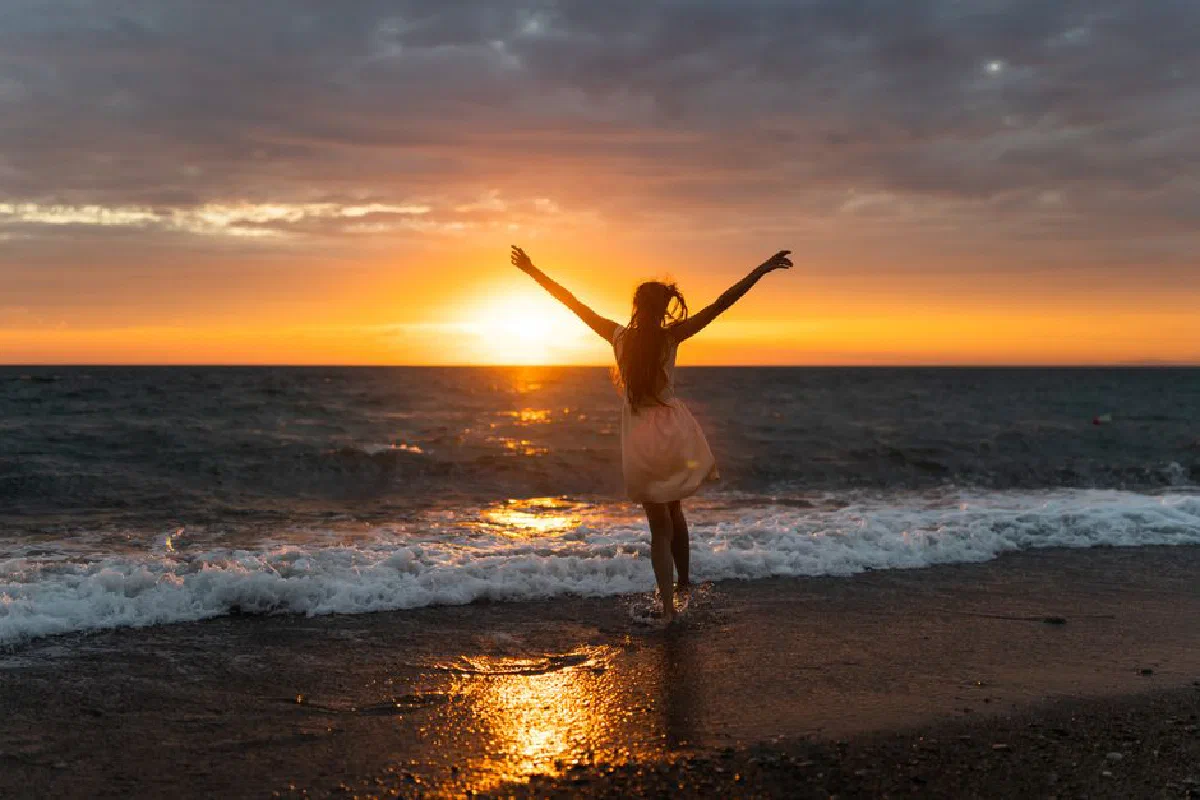 A woman joyfully celebrates freedom at sunset on Alakhadzi beach.