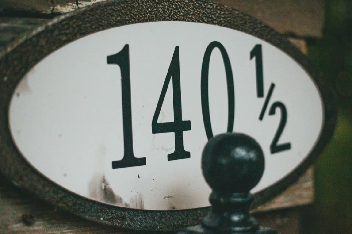 Close-up view of an old house number plate reading 140½ with a black decorative element.