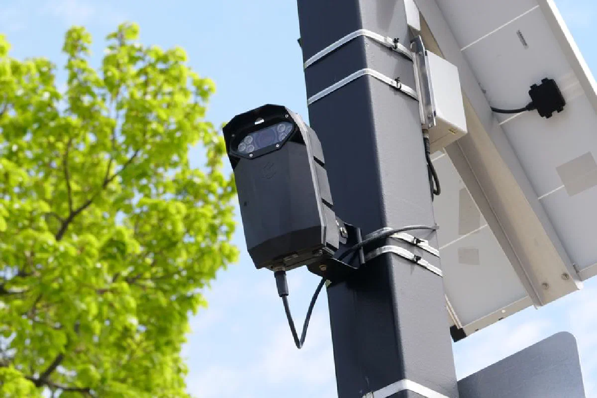 A modern surveillance camera powered by solar energy mounted on a street pole.