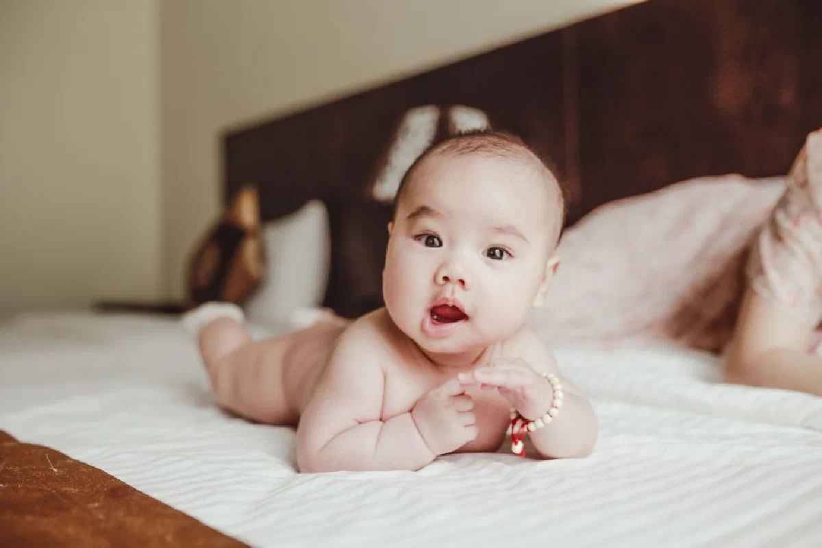 Charming baby lying on a bed, displaying innocence and joy in a cozy bedroom setting.
