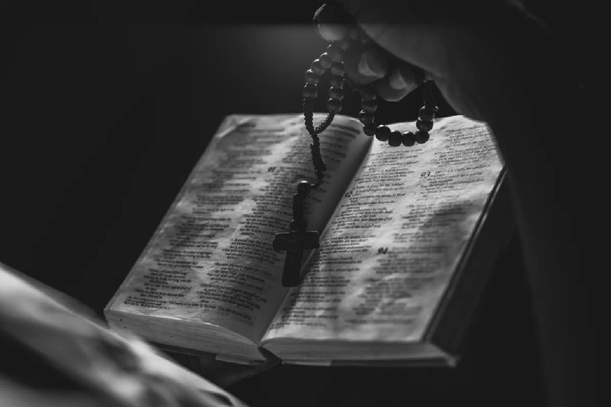 A black and white image of an open Bible with rosary beads, symbolizing faith and spirituality.