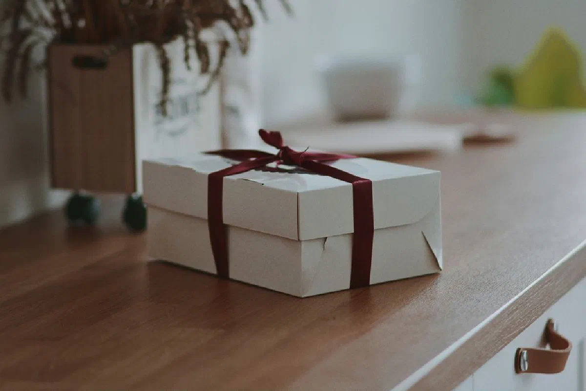 A white gift box with a red ribbon on a wooden surface, adding a touch of elegance and anticipation.