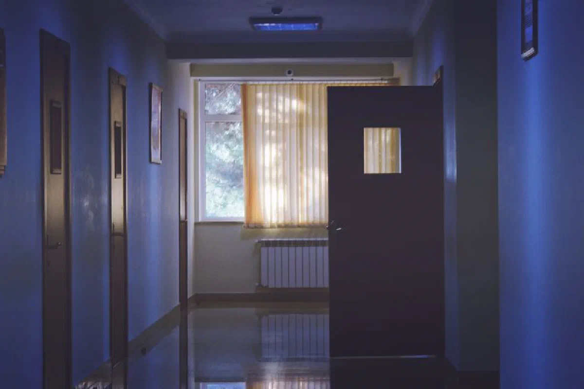 Dimly lit corridor with a window casting soft sunlight through blinds.