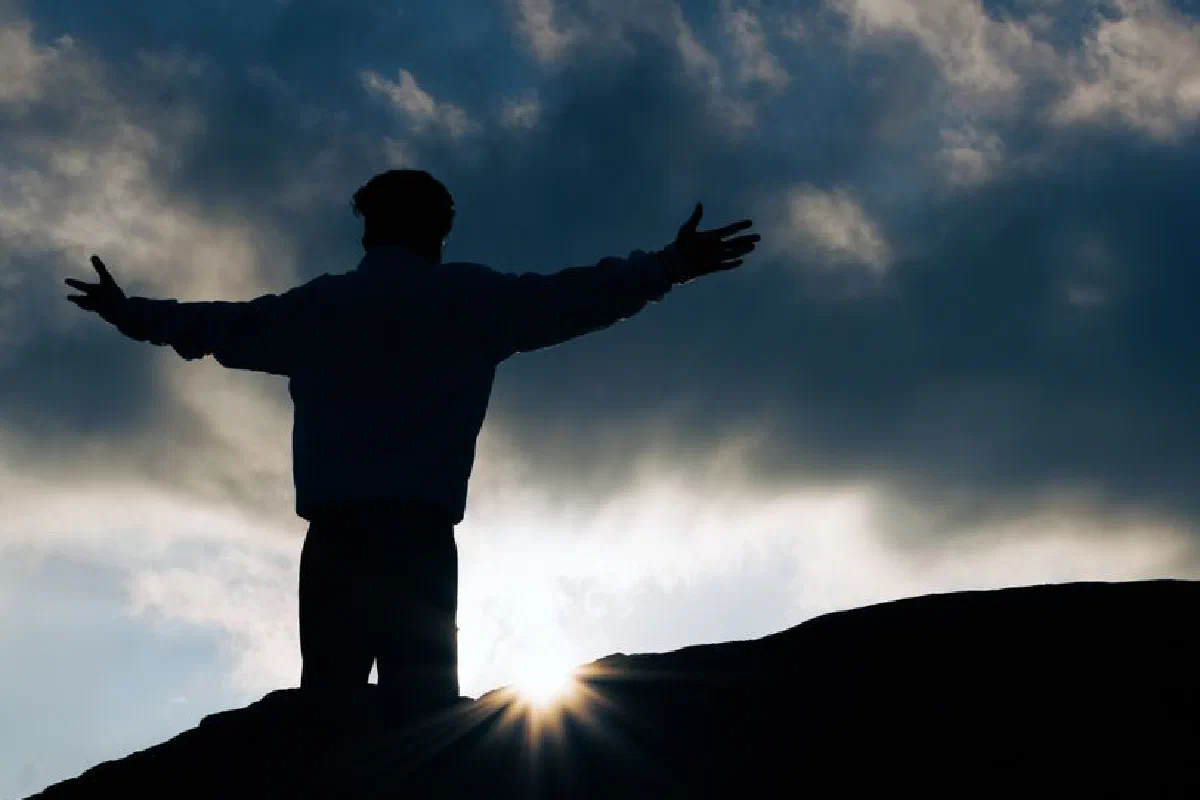 Silhouette view of a person with open arms at sunrise, symbolizing freedom and peace.