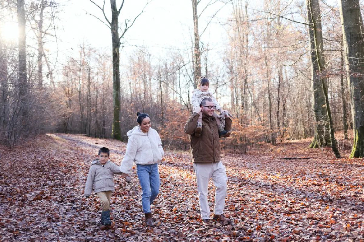 Family enjoying a walk in a forest with fallen leaves, capturing a warm, autumn moment.
