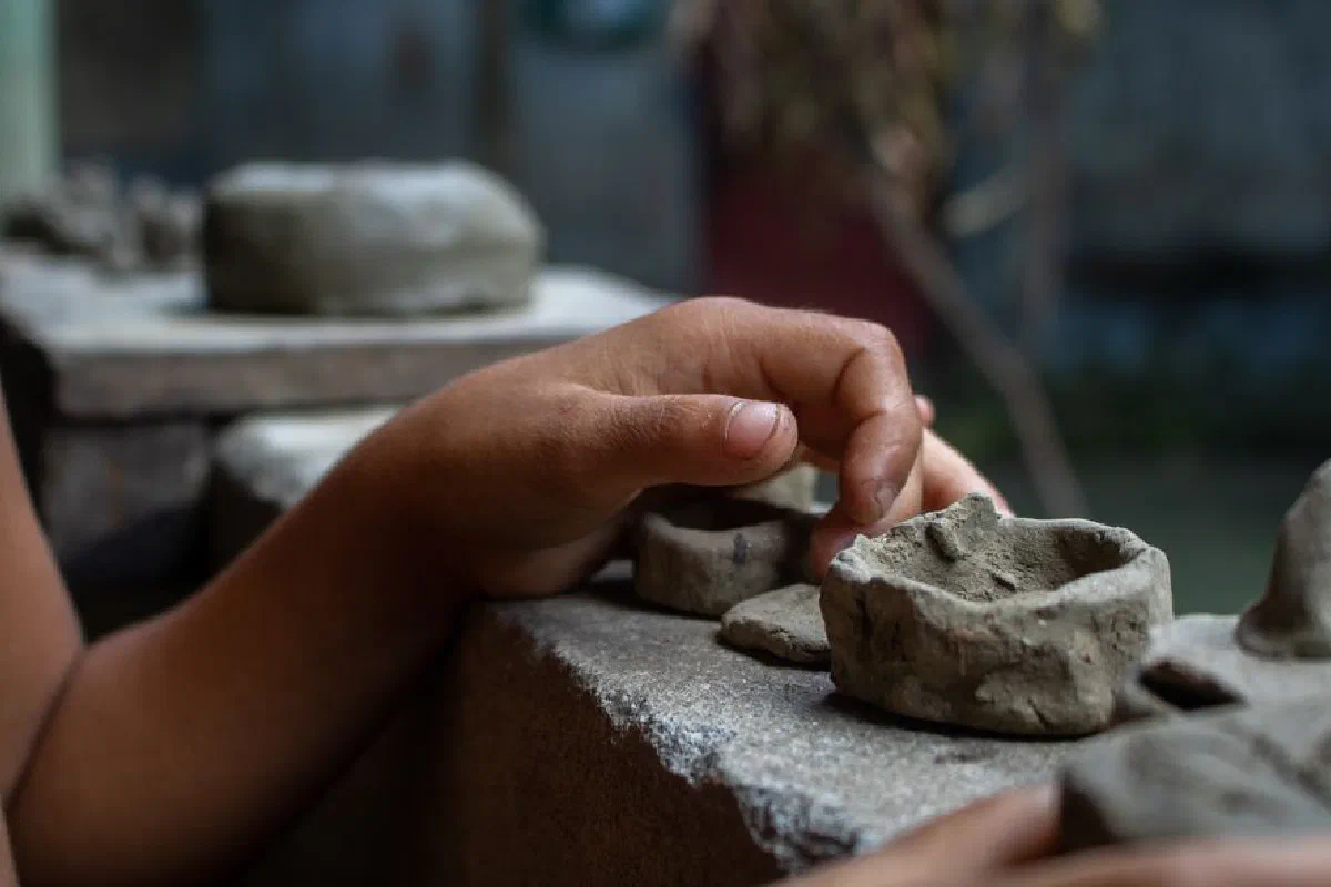 Close-up of a person shaping clay pottery outdoors, highlighting detailed craftsmanship.