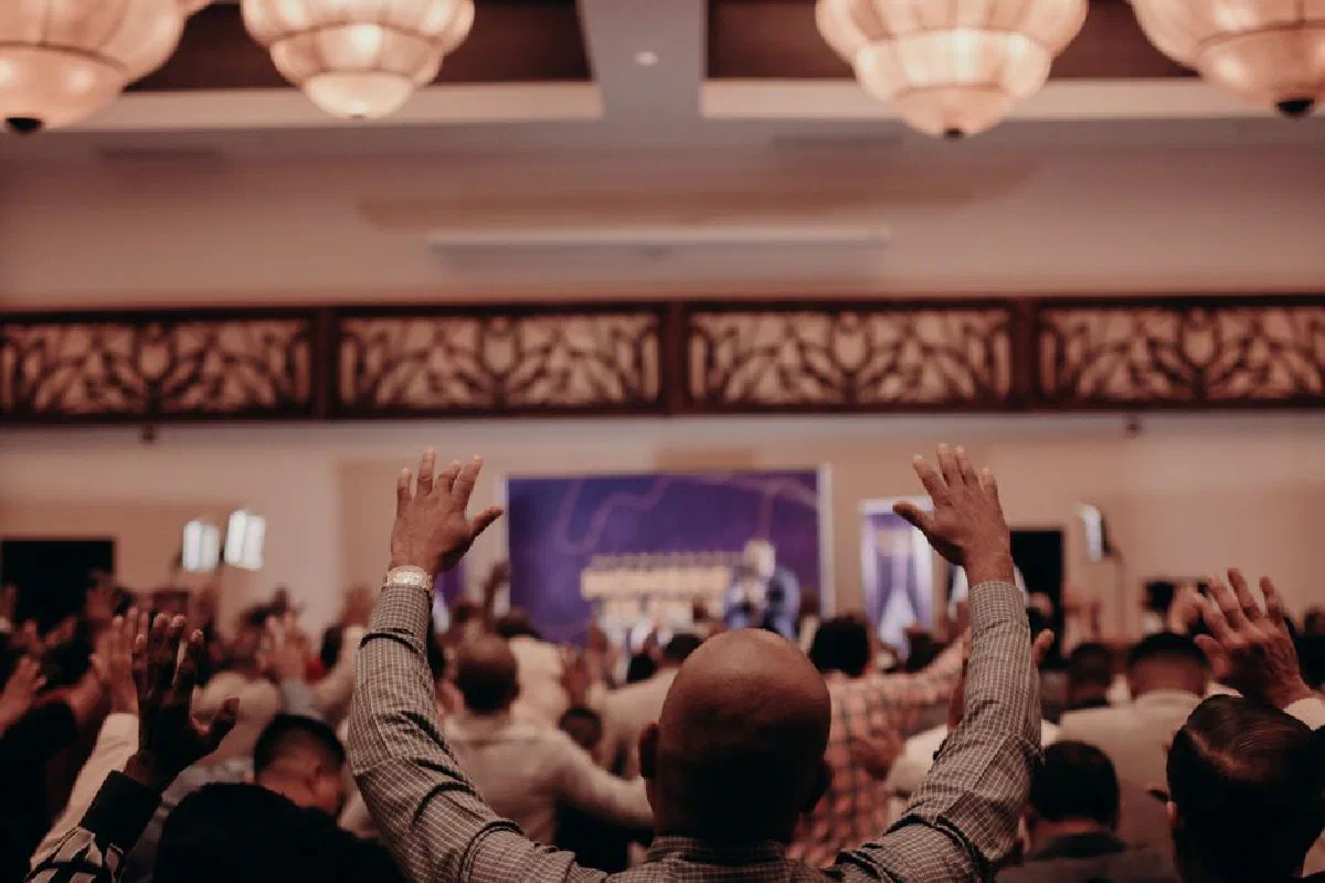 A dynamic crowd with raised hands in a richly lit indoor venue, capturing a moment of collective energy.