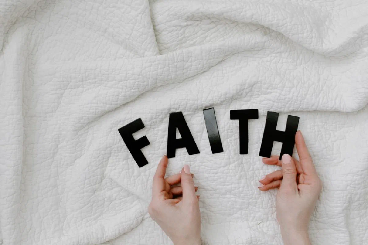 Hands arranging letters on a white quilt spelling FAITH. Minimal and serene concept.