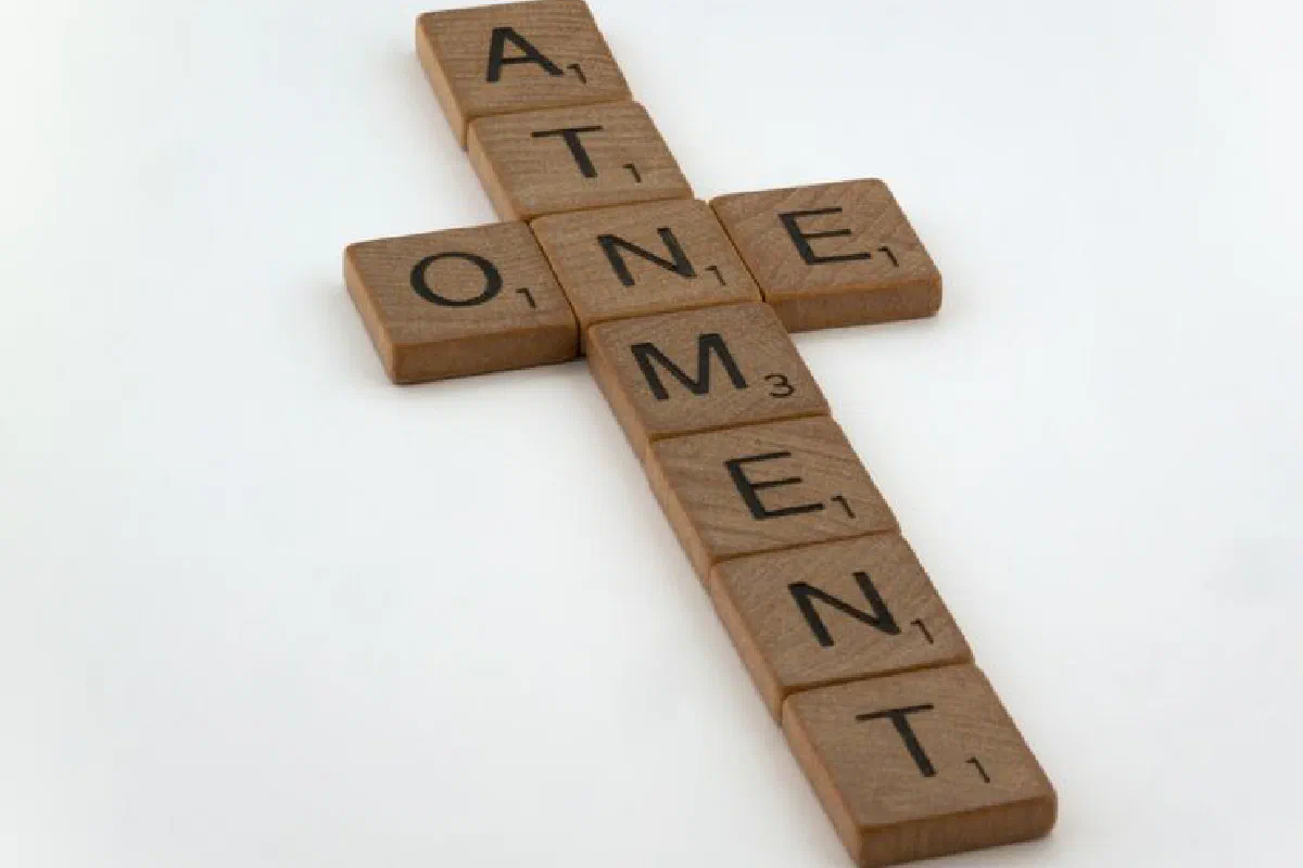 Scrabble tiles arranged in a cross shape spelling 'atonement' on a white background.