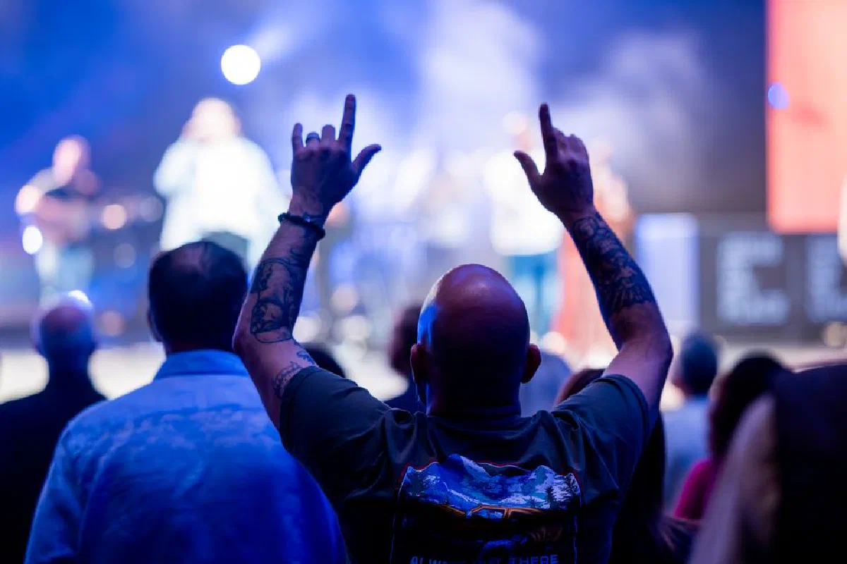 Bald man raises hands in excitement at a live concert. Vibrant stage lights.