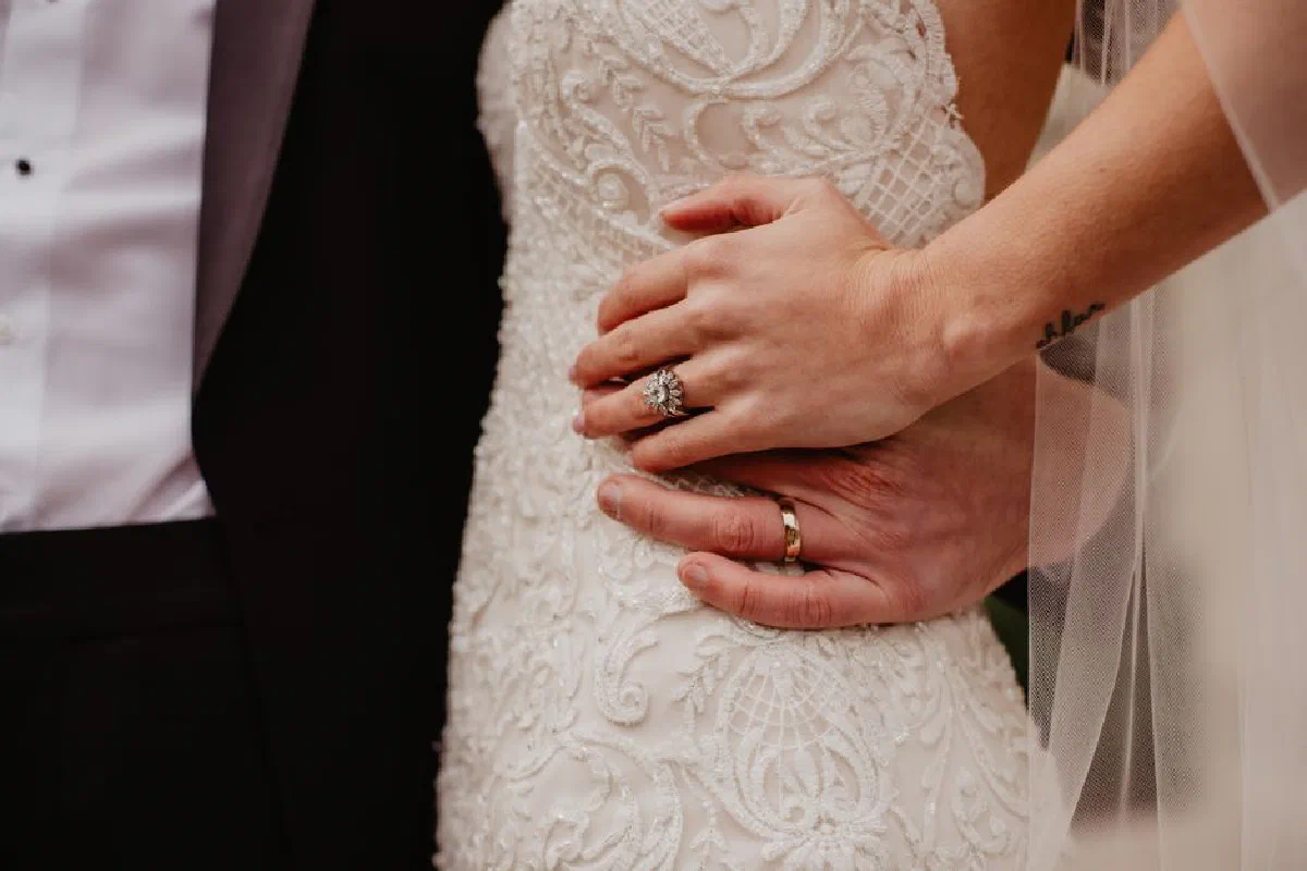 Close-up of a bride and groom embracing with focus on wedding rings and intricate dress details.