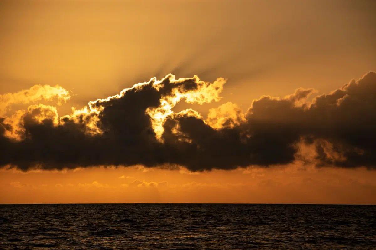 A beautiful sunset over the ocean with dramatic clouds and a golden sky.