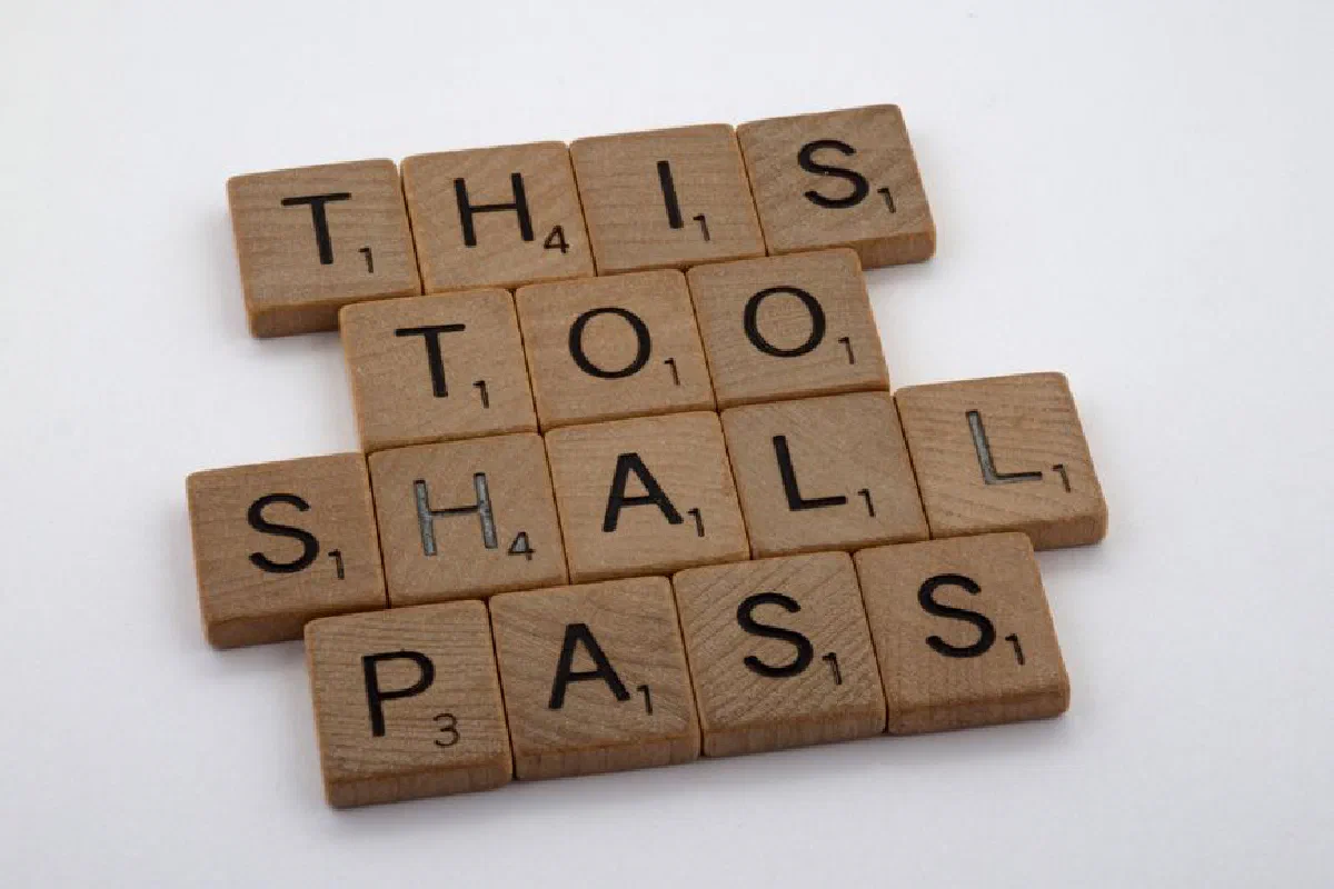 Wooden tiles form the motivational message 'This too shall pass,' highlighting resilience.