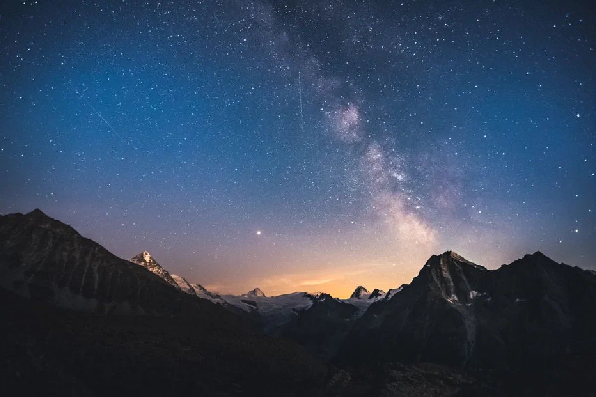 Captivating night sky over Swiss mountains featuring the Milky Way, offering a breathtaking view of stars and silhouettes.