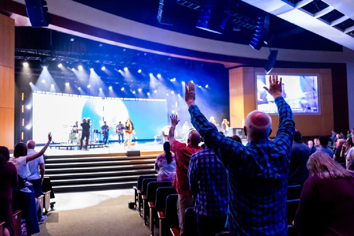 A lively worship service with an audience raising hands to a live band on stage in a church.