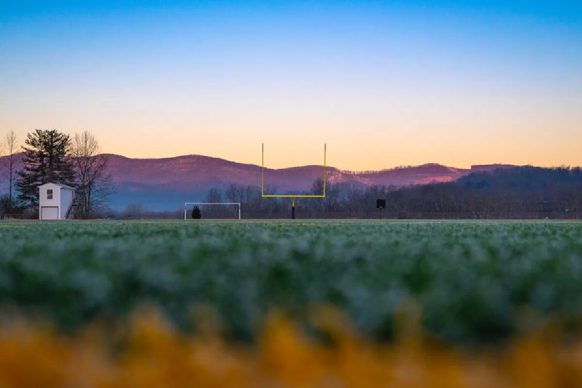A tranquil sports field at dawn with mountains in the background, enveloped in fog.
