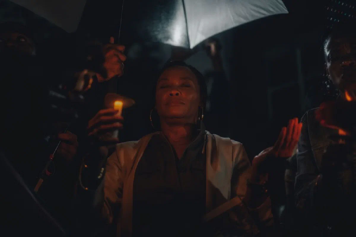 A serene candlelight vigil attendee with closed eyes holding a candle under an umbrella at night.