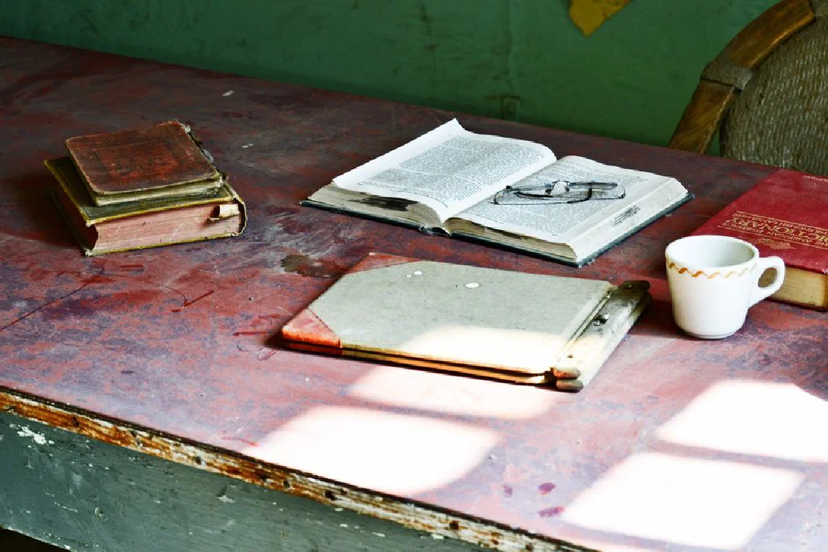 A rustic wooden desk with antique books, open text, and a cup, bathed in soft sunlight.