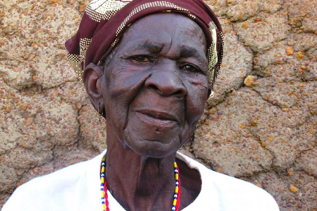 Elderly African woman wearing headscarf, portrait against textured wall outdoors in Fada-Ngourma, Burkina Faso.