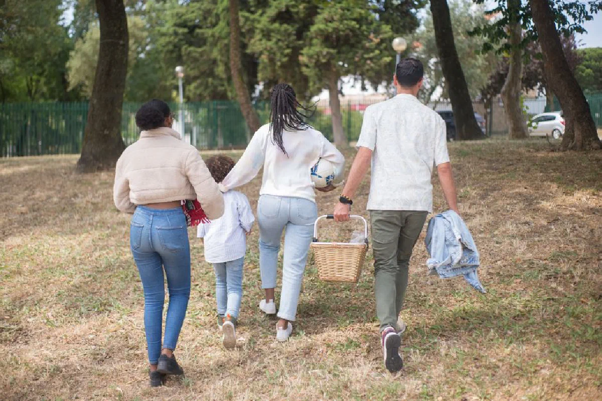 Family walking together carrying picnic basket in a sunny park.