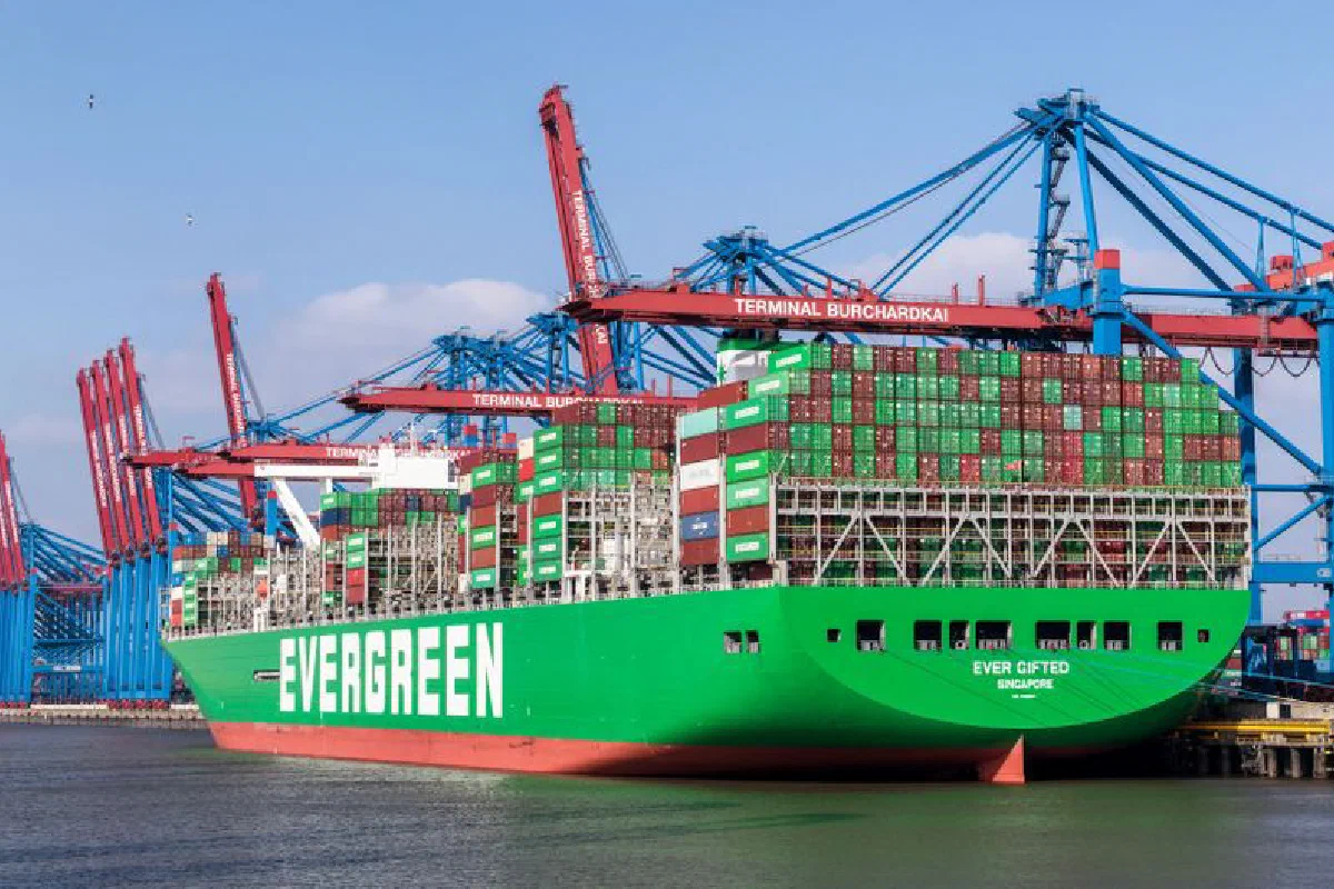 Evergreen cargo ship docked at Hamburg Harbor with cranes and blue sky.