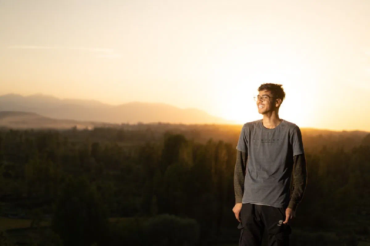 A young man smiles while standing outdoors at sunset in the lush forests near Srinagar.