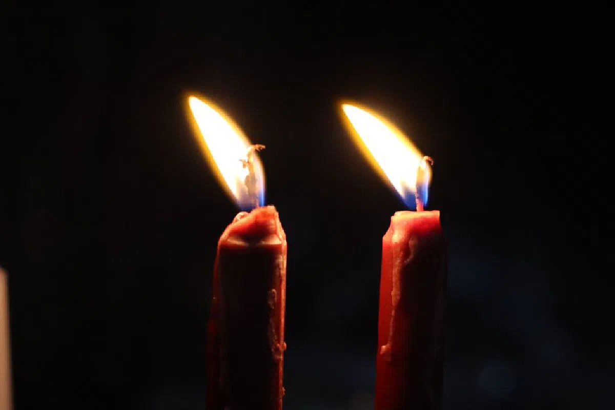 Warm glow of two lit candles casting light in darkness, symbolizing peace and spirituality.