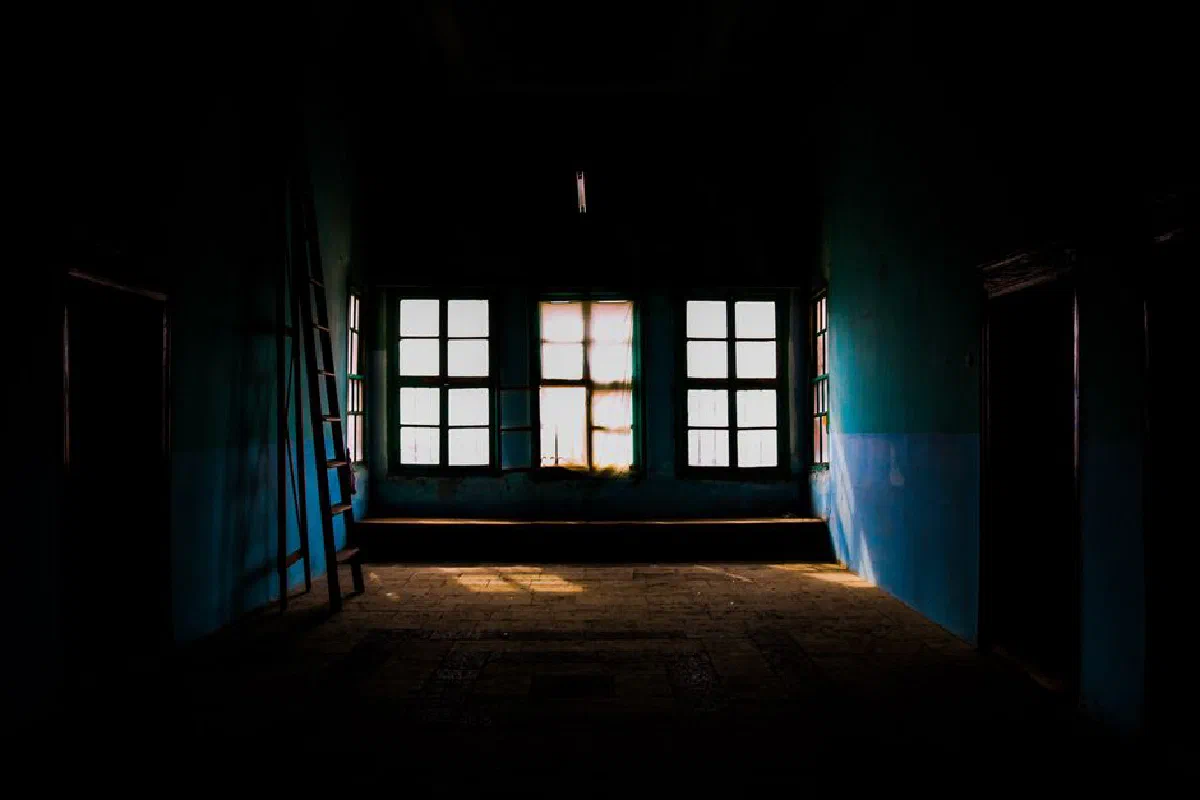Dark interior room with sunlight streaming through windows and a leaning ladder.