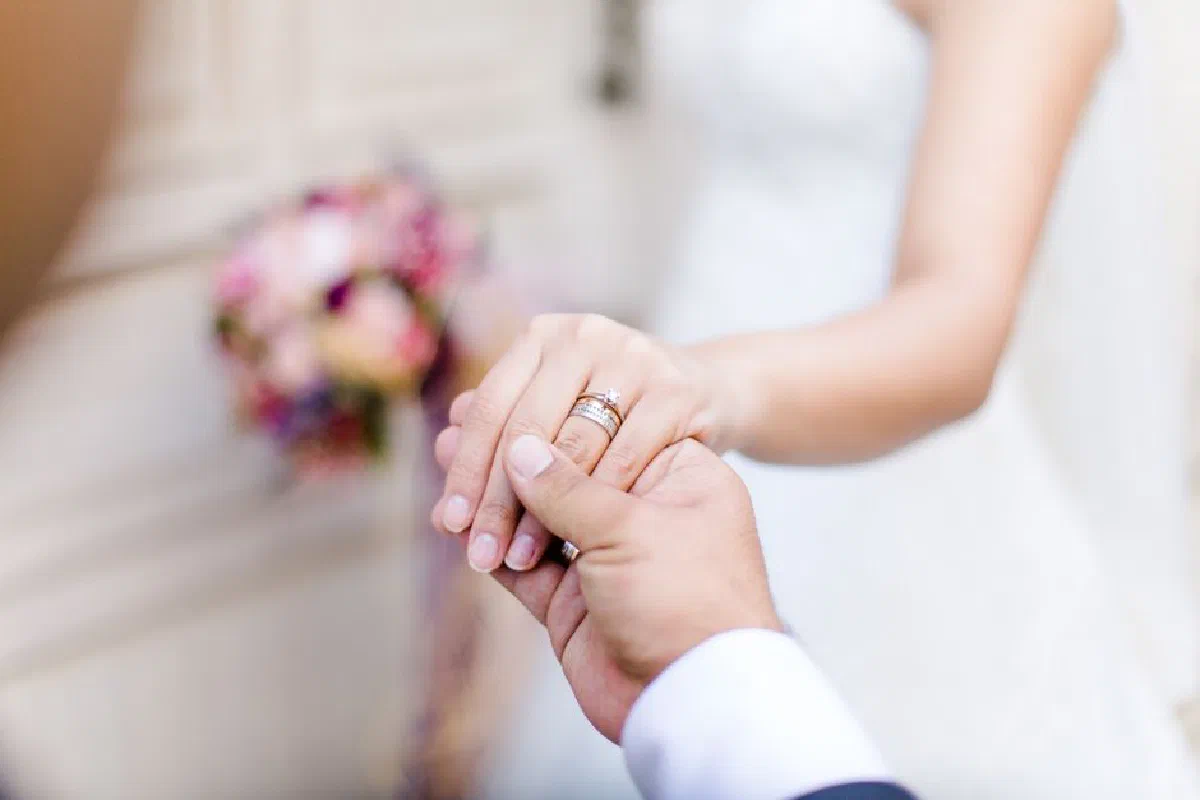 Bride and groom holding hands, focusing on wedding rings in a romantic moment.