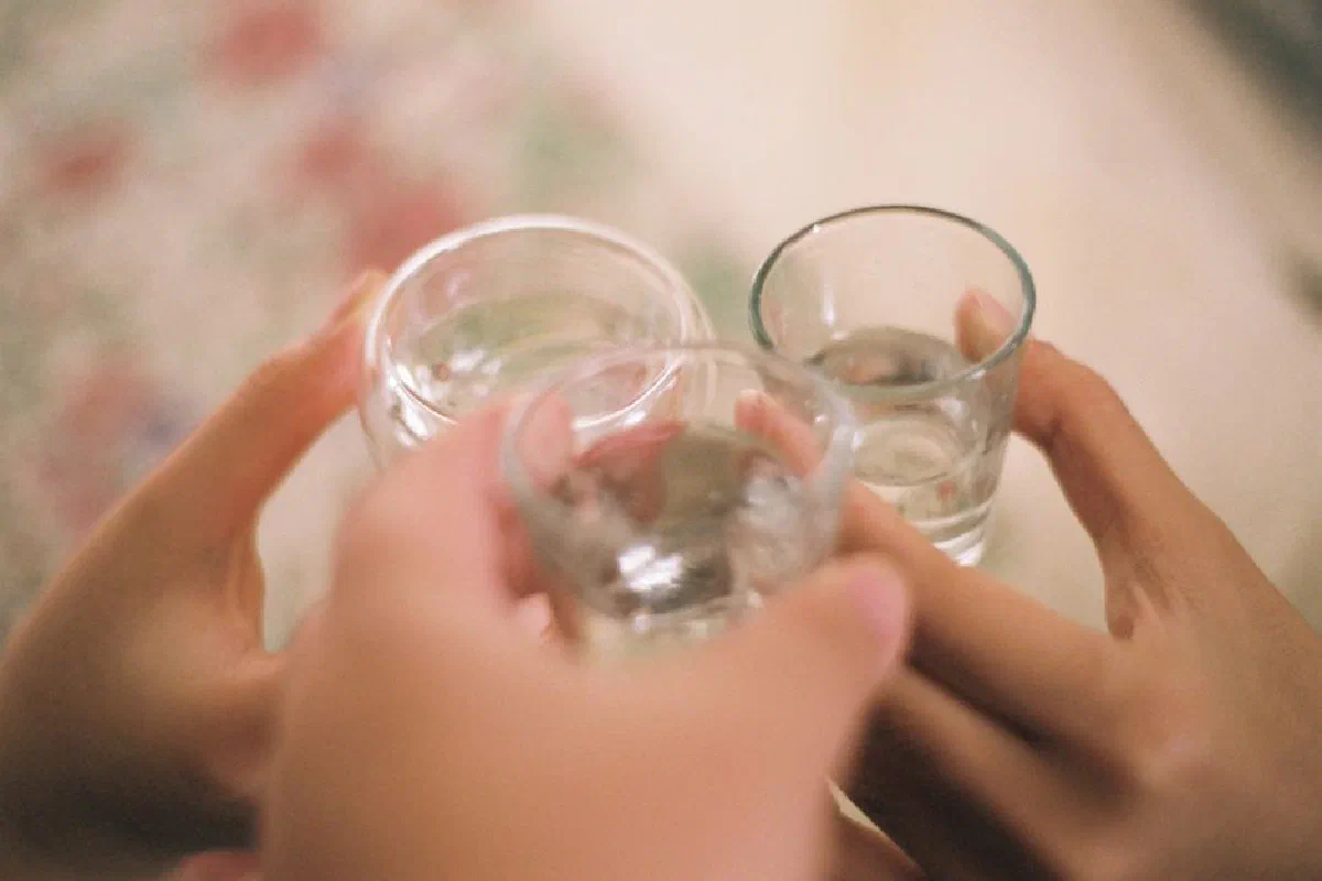 Three people clink glasses in a celebratory toast, highlighting a close-up view of hands and drinks.