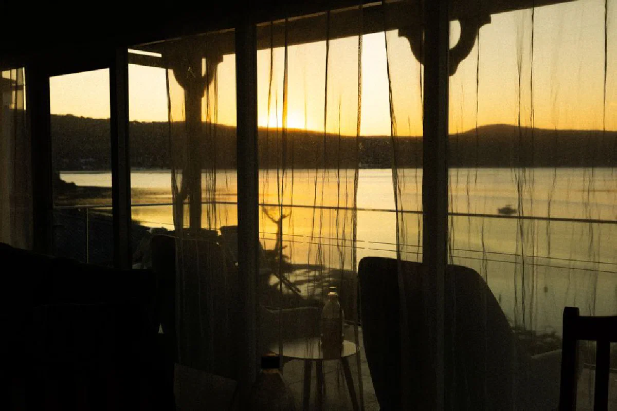 A peaceful sunset over a lake viewed through curtain-filtered windows, creating a cozy ambiance.