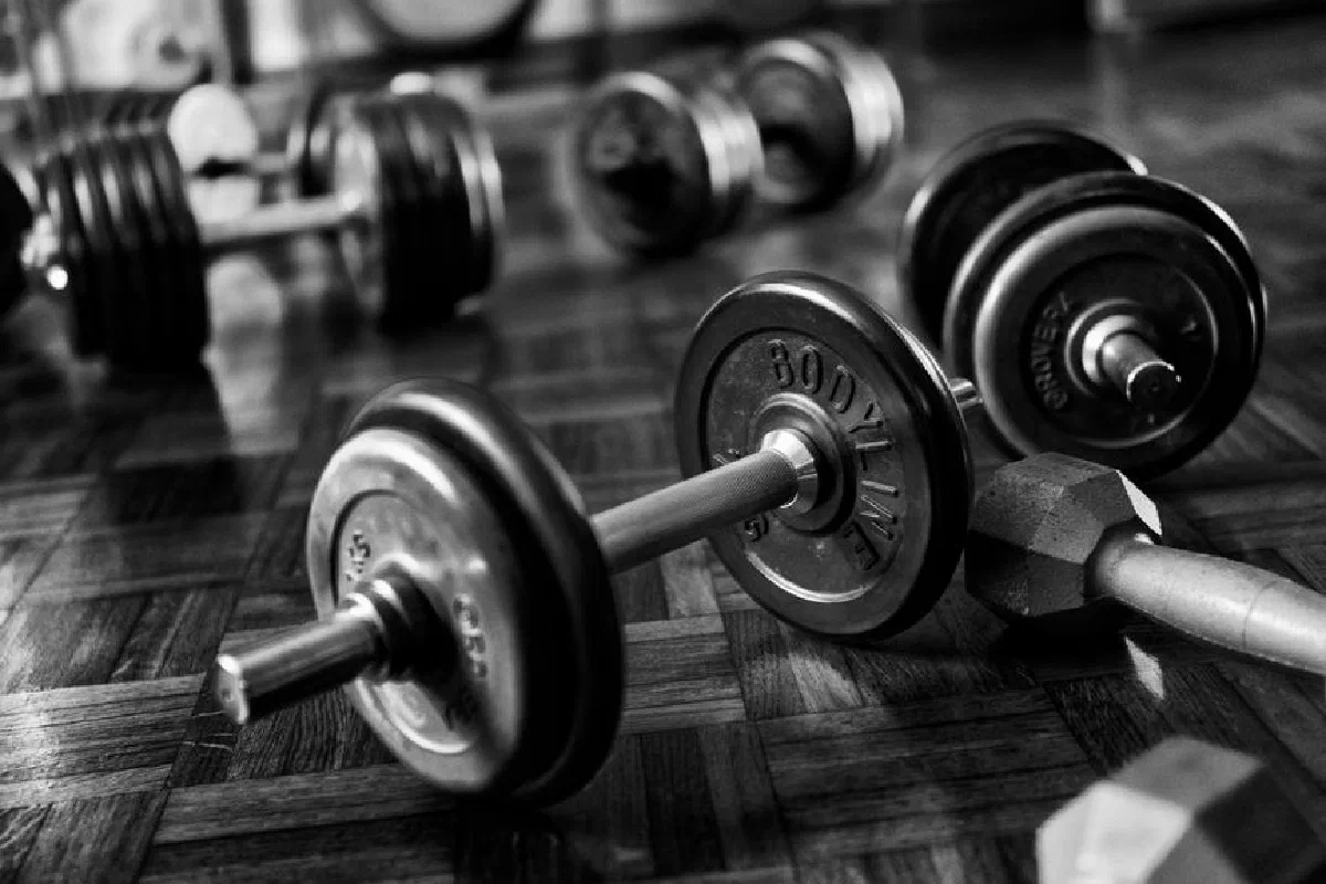 Black and white photo of gym dumbbells on a wooden floor, emphasizing strength and fitness.