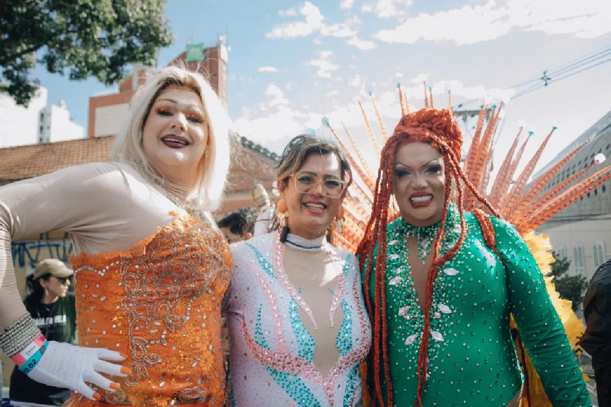 Three drag queens in colorful costumes enjoying an outdoor celebration.