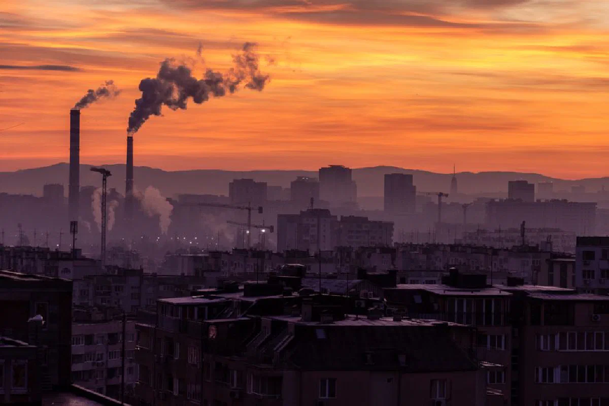 A city skyline with smokestacks emitting pollution, set against a vibrant sunset sky.