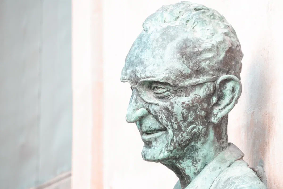 Sculpted bronze bust of an elderly man with glasses, displaying weathered details and classical art style.