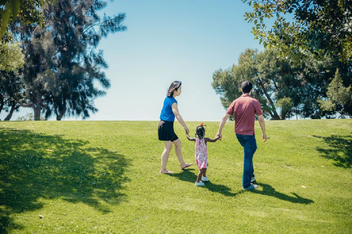 A family walks hand in hand in a sunny park, enjoying nature and togetherness.