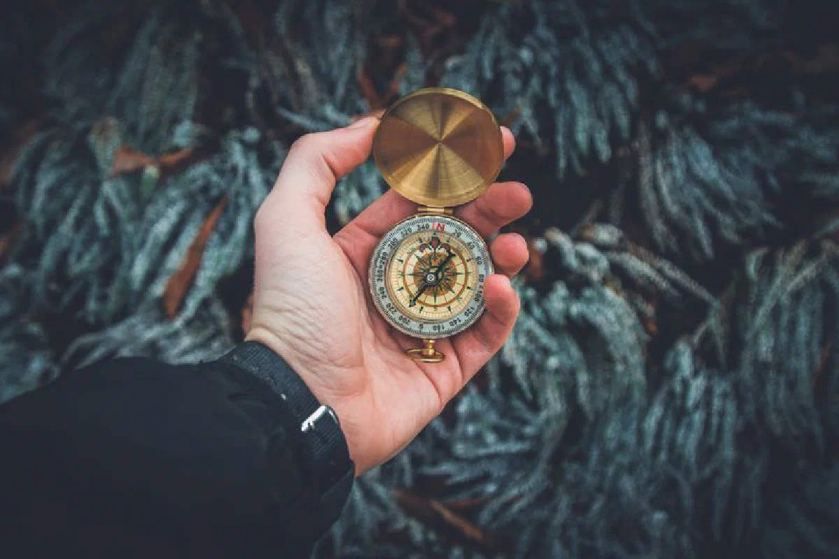 A close-up shot of a hand holding a vintage compass against a natural background.